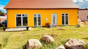 A yellow building with a red roof, large windows, and a grassy yard with rocks. - The yellow house at the harbor (Wolgast)