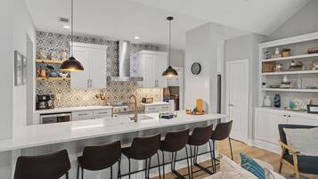 A modern kitchen with a central island, bar stools, pendant lighting, and a decorative backsplash.
