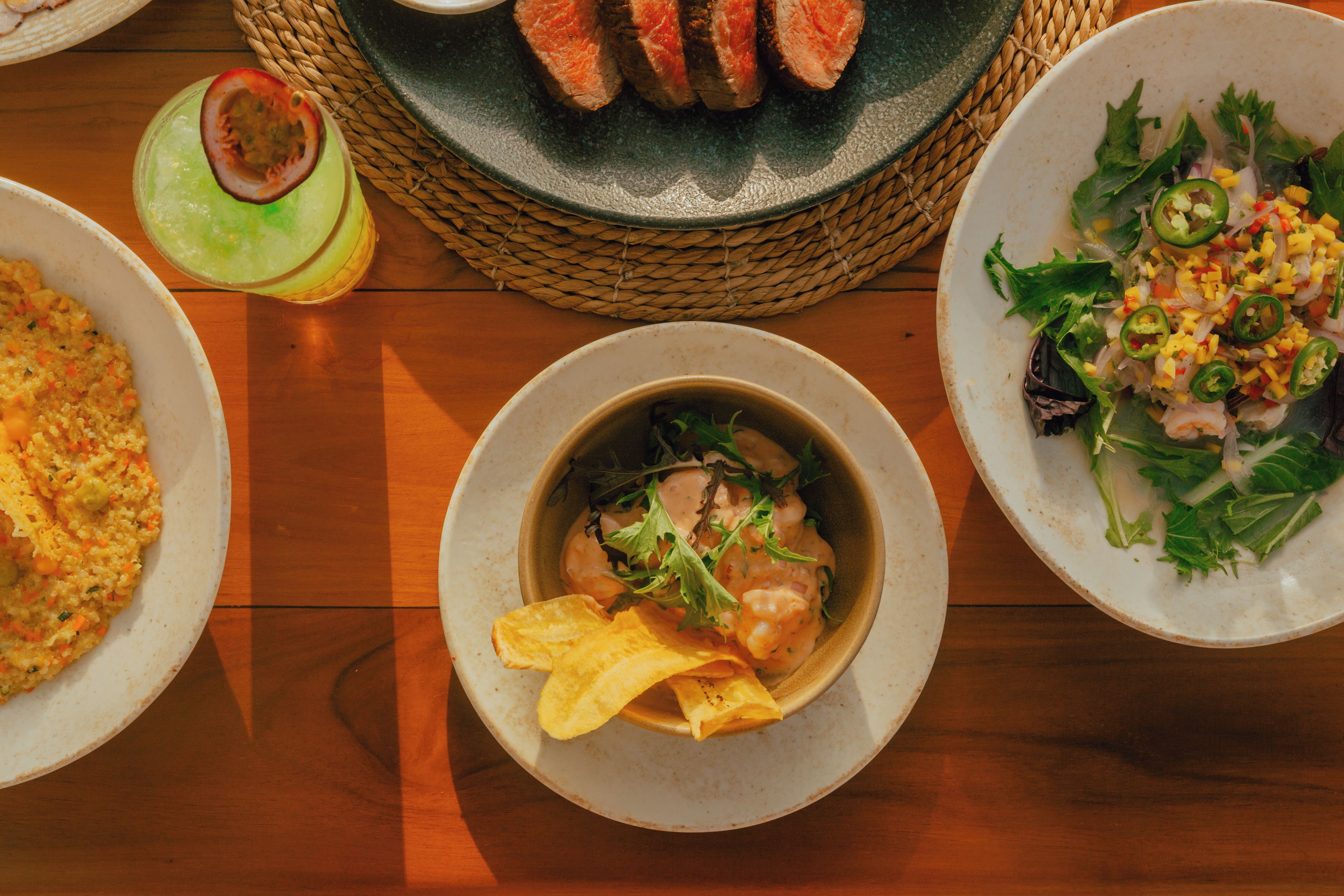 Une table où l’on trouve différents plats, notamment un bol de soupe accompagné de pain, une assiette de viande tranchée et une salade de légumes.