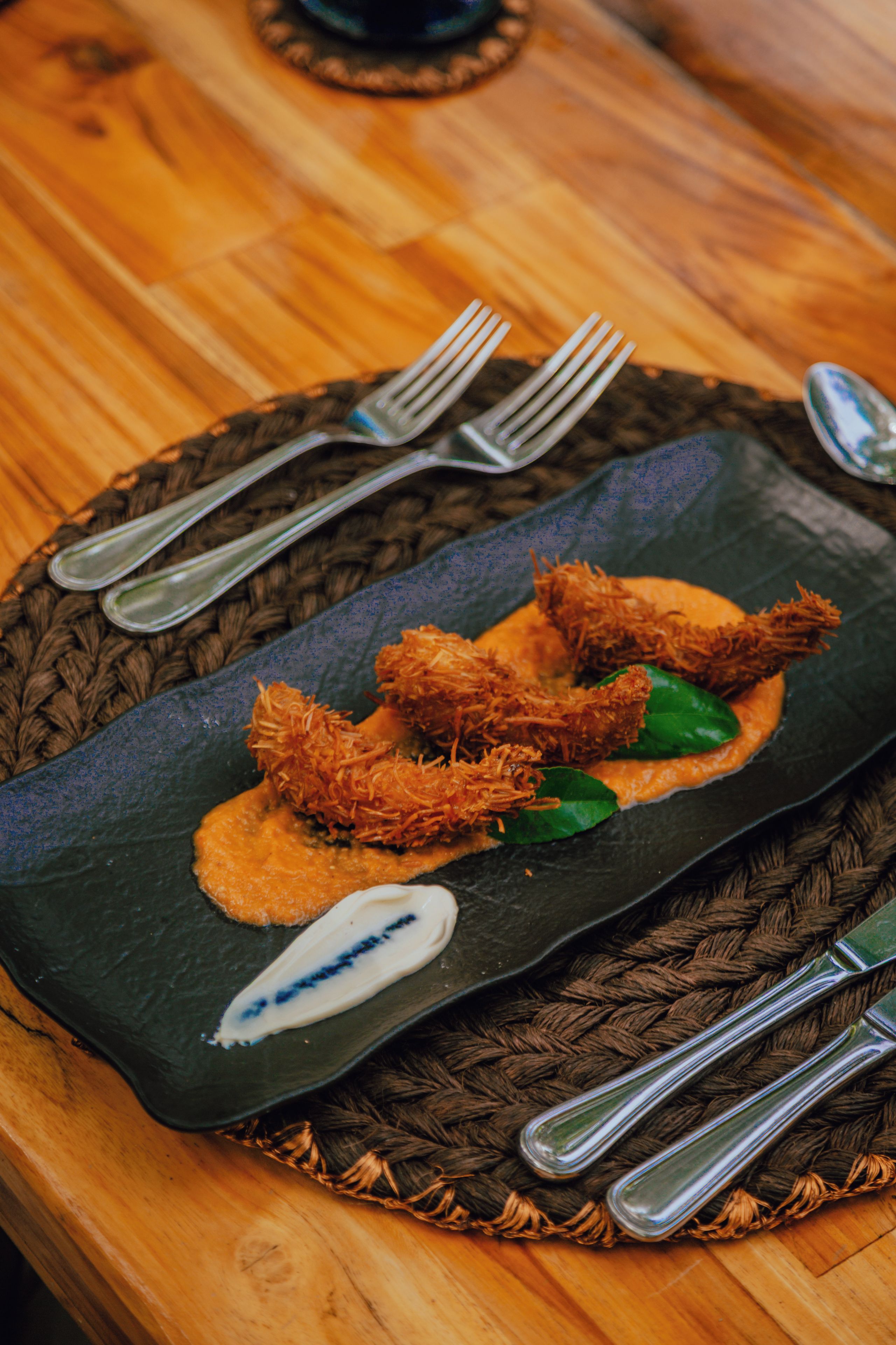 Une assiette rectangulaire contenant une sauce foncée, deux portions de nourriture frite et une cuillerée de sauce blanche, le tout disposé sur un napperon.