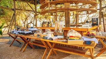 An outdoor dining area with wooden tables and chairs, surrounded by a bamboo structure.