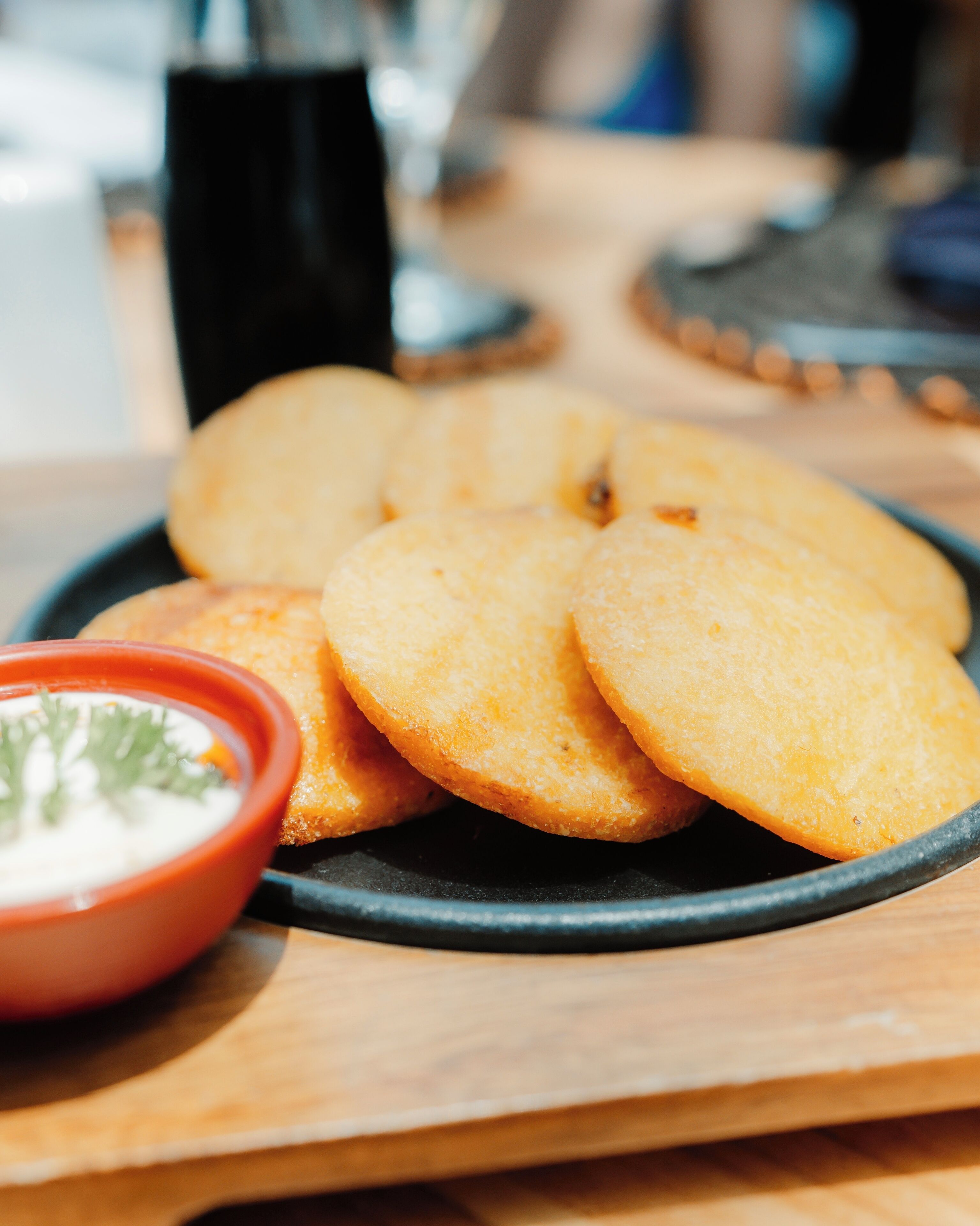 A plate of golden-brown fried items, possibly fritters, accompanied by a small bowl of white dipping sauce.