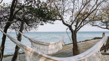 Un hamac est tendu entre deux arbres sur une plage de sable, avec l’océan en arrière-plan.