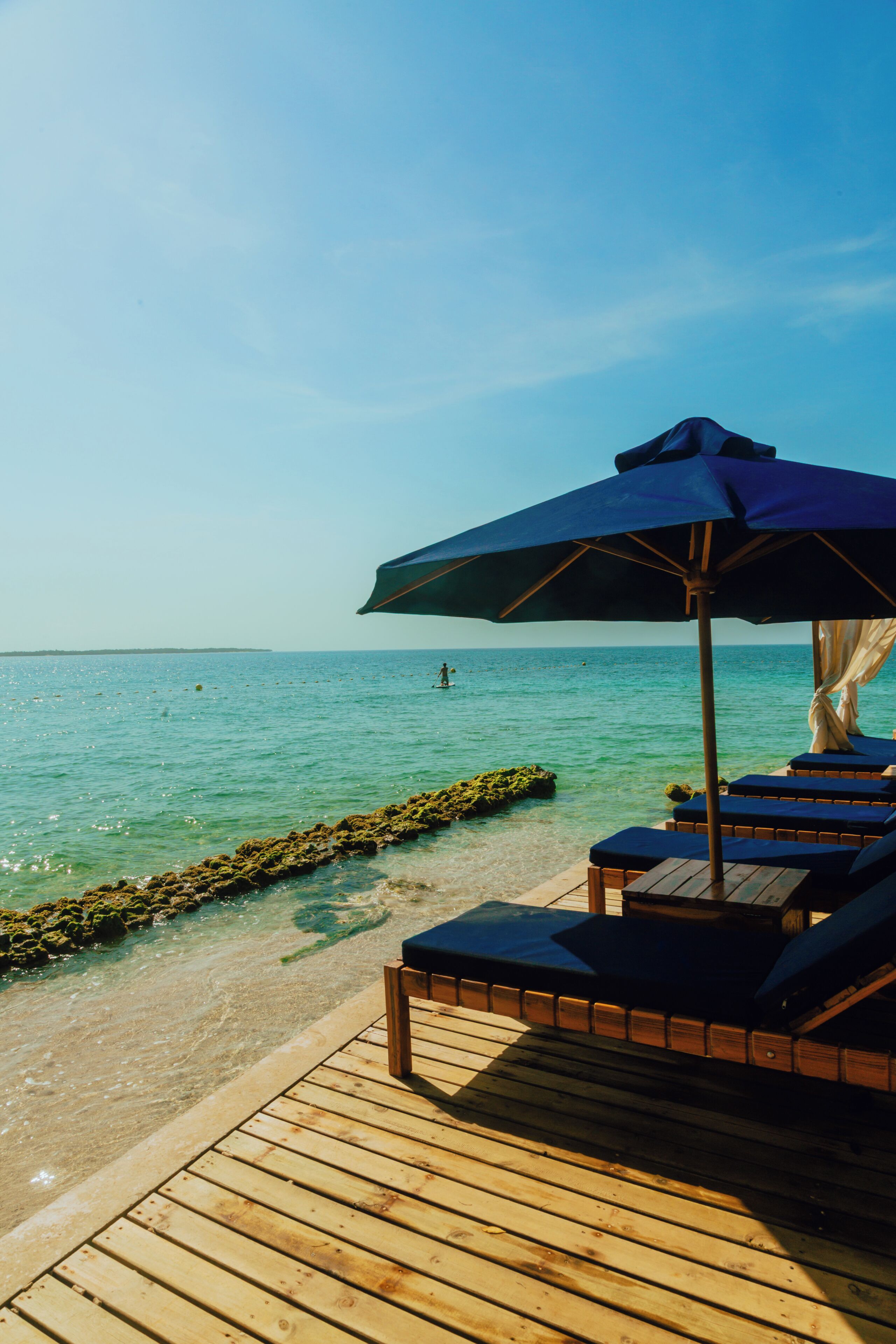 Een houten terras met ligstoelen en een grote parasol.