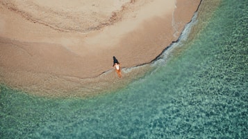 Vista aérea de una playa con aguas poco profundas y cristalinas, y una persona caminando por la orilla.