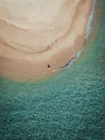 Vista aérea de una playa con aguas poco profundas y cristalinas, y una persona caminando por la orilla.