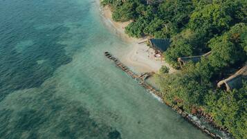 An aerial view of a beach with clear turquoise waters, a wooden walkway, and dense green foliage.