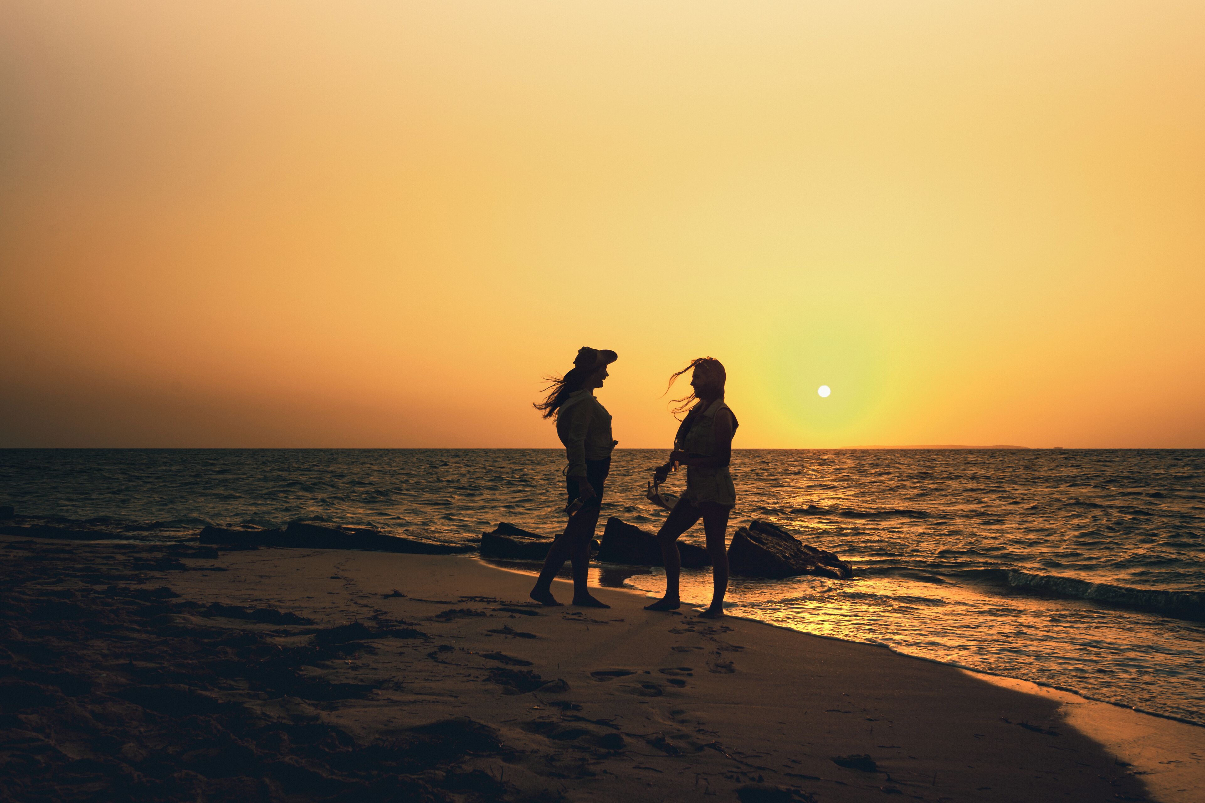 Two people walking on a beach at sunset.