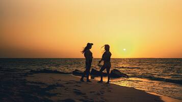 Two people walking on a beach at sunset.