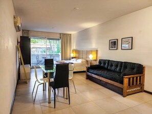 Relax in this stylish living room with a glass dining table, comfortable sofa, and a bed with a wooden headboard.