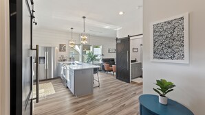 A modern kitchen with a central island, stainless steel appliances, pendant lighting, and a 'WELCOME' sign.