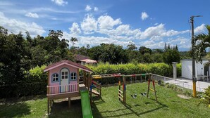 A children's play area with a slide, swings, and a small house structure. - Colina del Sol Hotel Hacienda (Quimbaya)