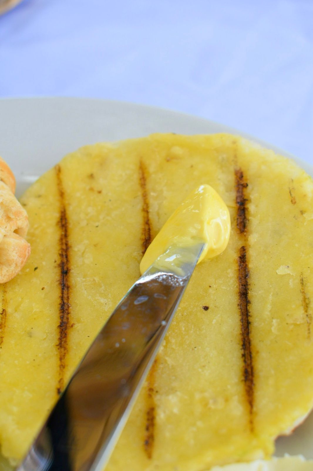 A close-up of a grilled yellow food item with a knife on it.