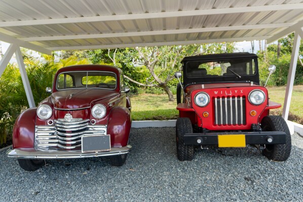 Two vintage cars parked under a covered area with gravel ground.