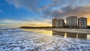 Un hotel frente a la playa con varios edificios altos, una playa de arena y olas oceánicas.