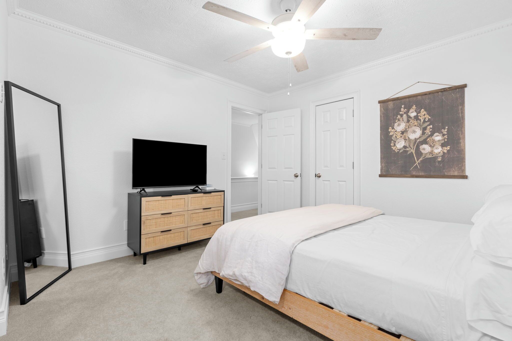 A bedroom with a bed, a dresser, a television, a ceiling fan, and a wall-mounted artwork.