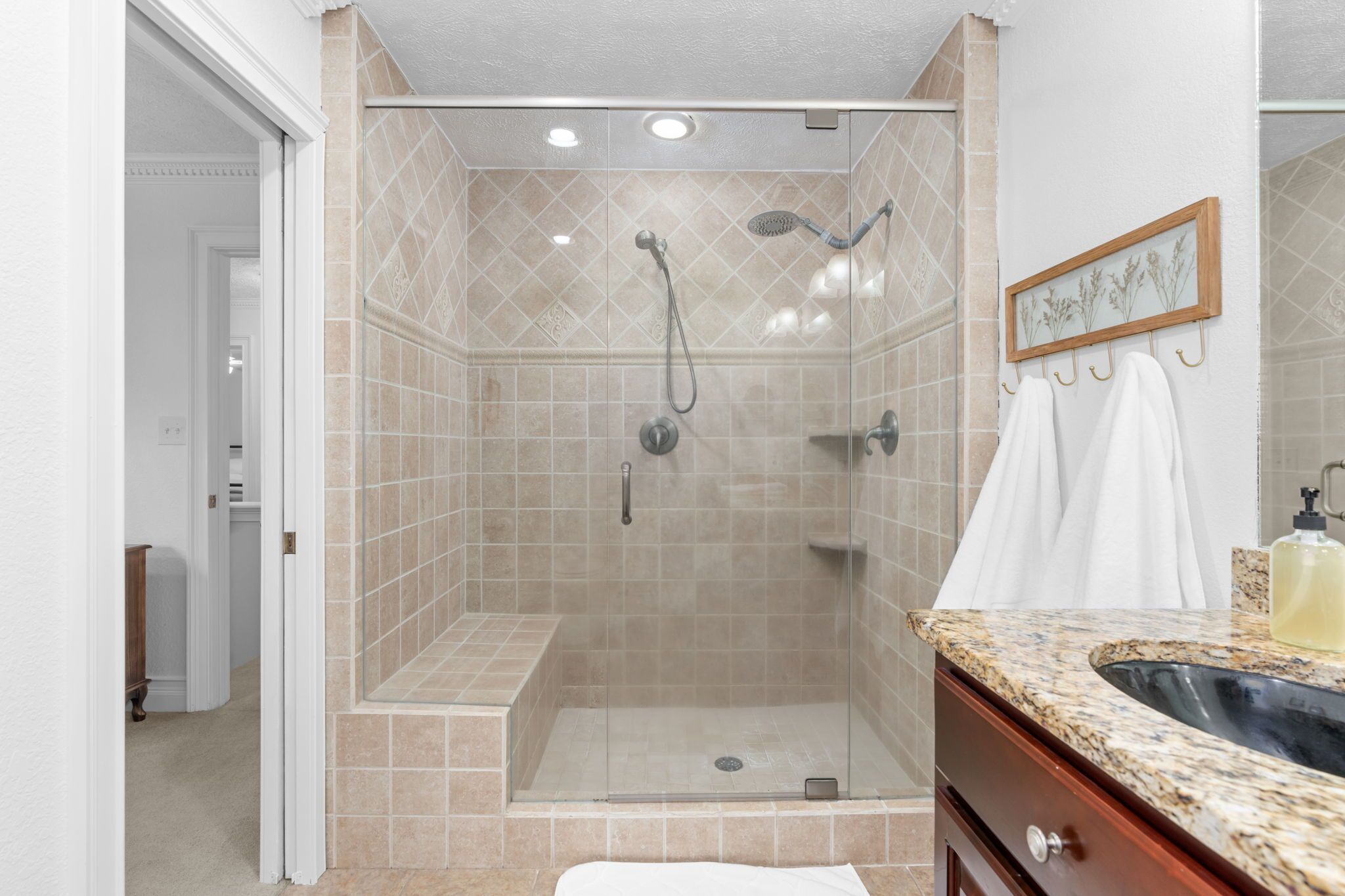 A walk-in shower with beige tiles, a glass door, and a wooden frame with towels.