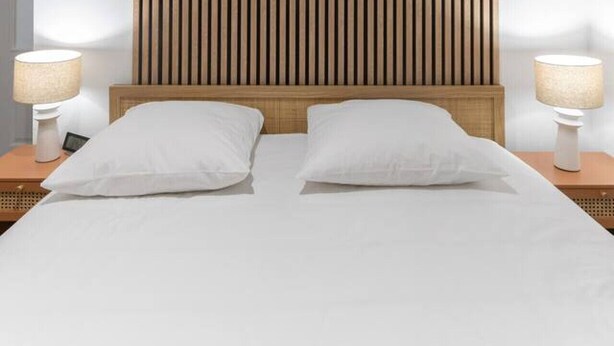 A modern bedroom with a wooden slatted headboard, a large bed with white linens, and two bedside lamps. - Le Serbie RdC - 4 rue de Serbie - Vichy (Vichy)