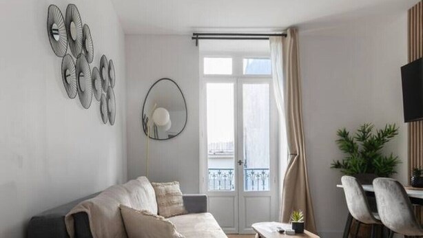 Een moderne woonkamer met een grijze bank, een ronde salontafel en een eethoek met stoelen en een televisie.