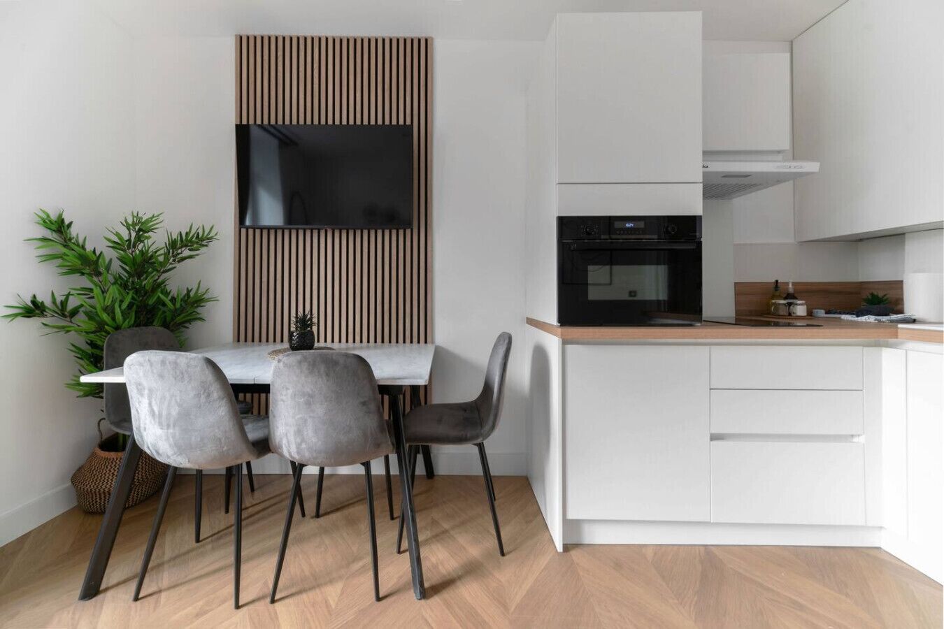 Eine moderne Küche mit Einbauofen, weißen Schränken und einem Holzespeisetisch mit vier Stühlen.