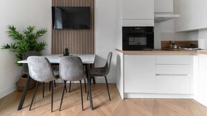 Een moderne keuken met een inbouwoven, witte keukenkastjes en een houten eettafel met vier stoelen.
