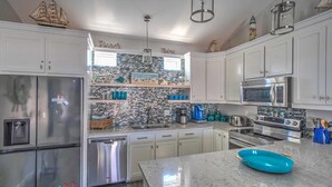 A modern kitchen with stainless steel appliances, white cabinetry, and a backsplash with a mosaic tile design.