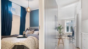Ein Schlafzimmer mit Bett, Nachttisch und Vorhängen. Das Zimmer hat ein Fenster und eine Tür.