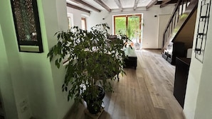 A spacious living area with a large potted plant, wooden flooring, and a staircase leading to an upper level. - Au moulin - GEX - Gîte (GEX)