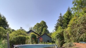 A rectangular swimming pool with a clear blue water surface, surrounded by a stone border and a wooden deck. - Au moulin - GEX - Gîte (GEX)