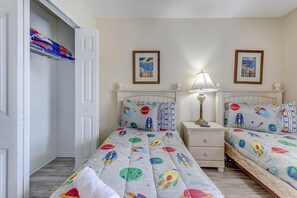 Ein Schlafzimmer mit zwei Betten, jedes mit einer Bettdecke mit Weltall-Motiv, einem Nachttisch mit Lampe und einer Tür zu einem Schrank.