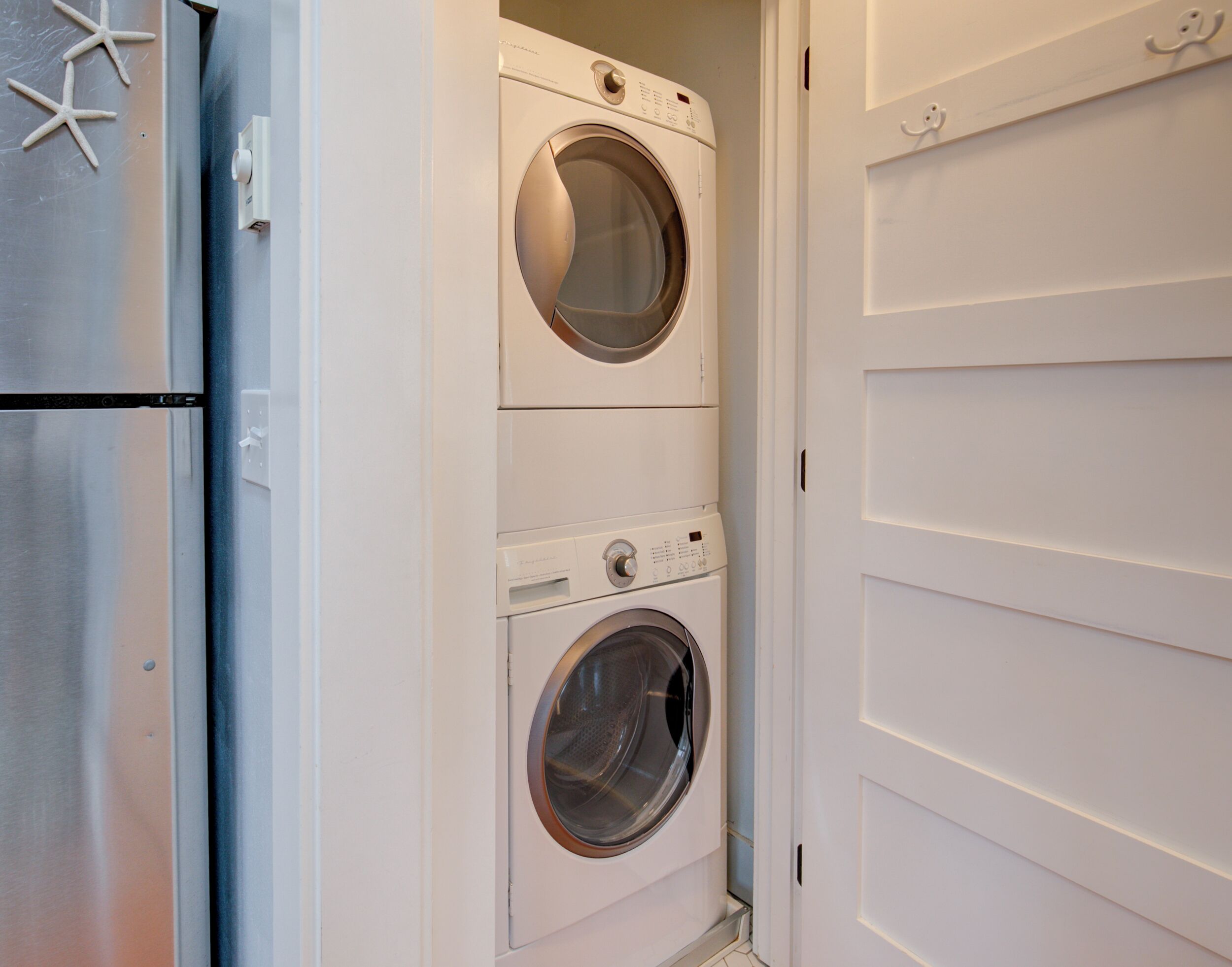 A compact laundry room with a front-loading washer and dryer, a stainless steel refrigerator, and a white door with a simple handle.