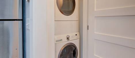 A compact laundry room with a front-loading washer and dryer, a stainless steel refrigerator, and a white door with a simple handle.
