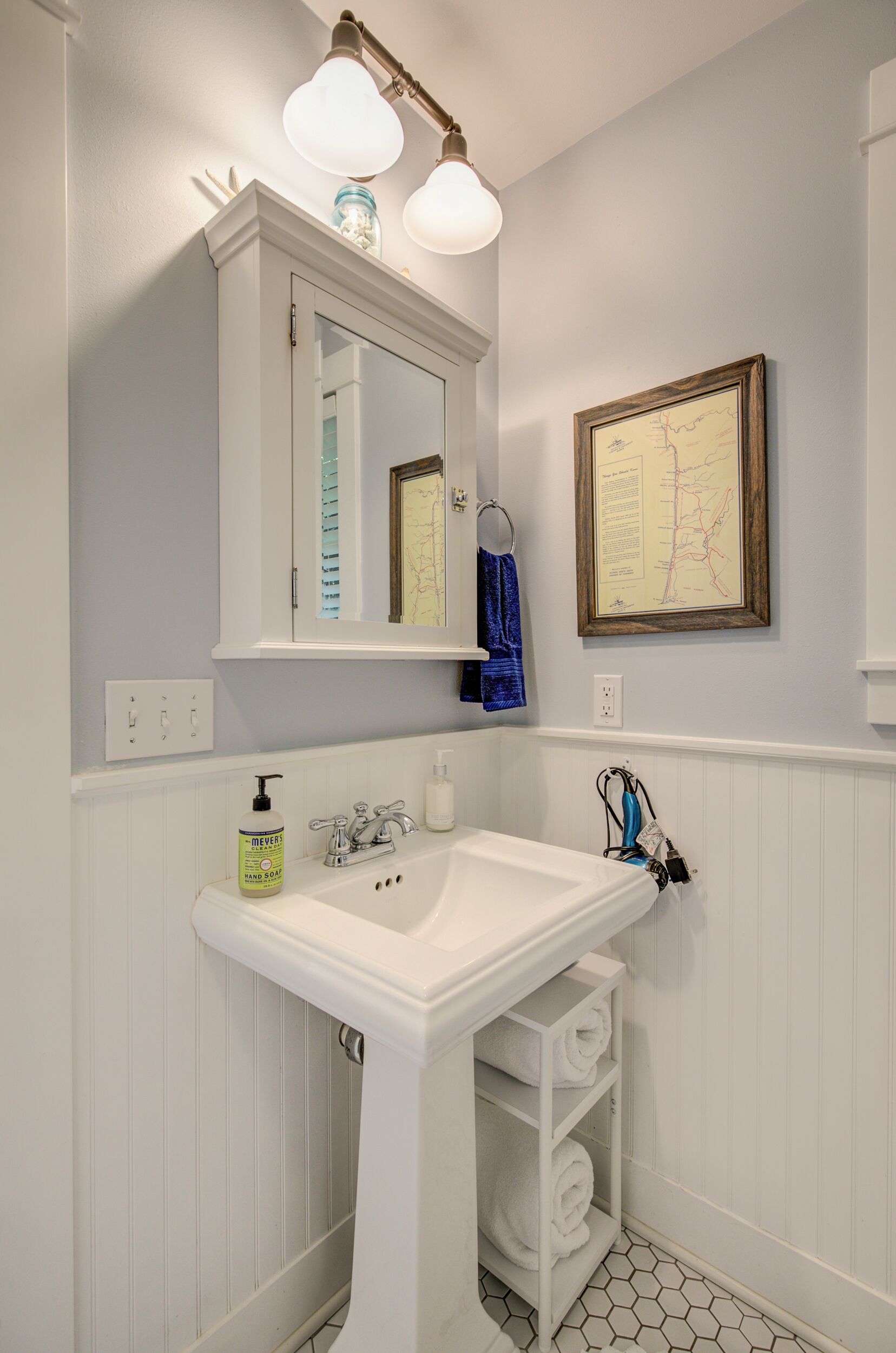 A bathroom with a white vanity, a mirror above the sink, a framed map on the wall, and a towel rack.