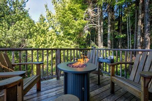 A wooden deck with a fire pit in the center, surrounded by wooden chairs.