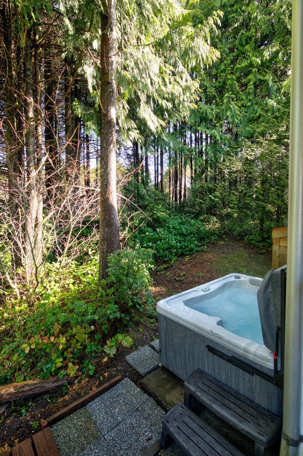 A hot tub in a forested area with a wooden deck and stone steps leading to it.