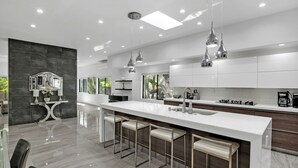 A modern kitchen with a large island, bar stools, pendant lighting, and a view of the outdoors.