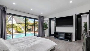 A modern bedroom with a large bed, a TV, and a sliding glass door leading to a pool.