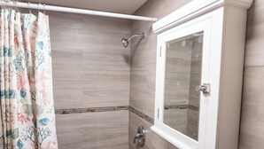 Une douche avec un sol en bois, une porte en verre et un meuble blanc avec un miroir.