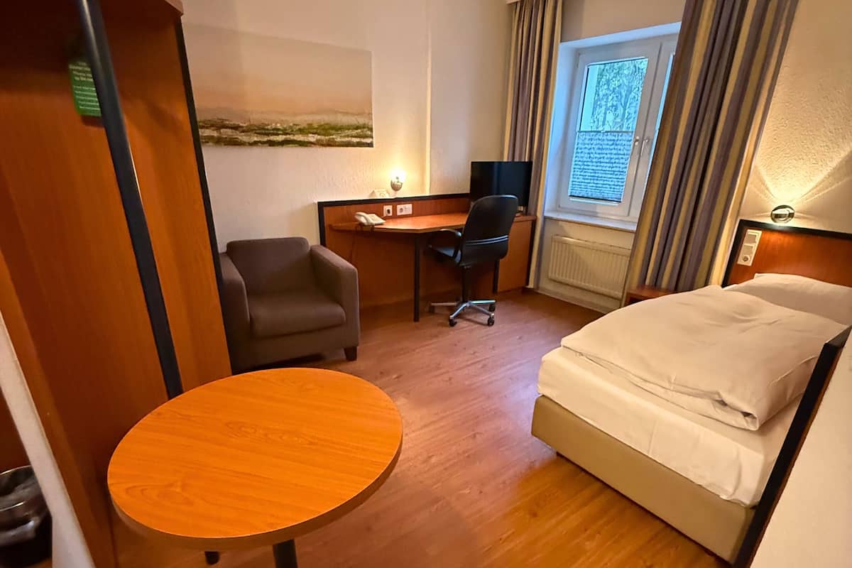 A hotel room with a bed, a desk, a chair, a small round table, and a window with curtains.