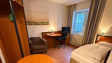 A hotel room with a bed, a desk, a chair, a small round table, and a window with curtains.