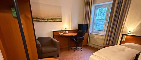 A hotel room with a bed, a desk, a chair, a small round table, and a window with curtains.