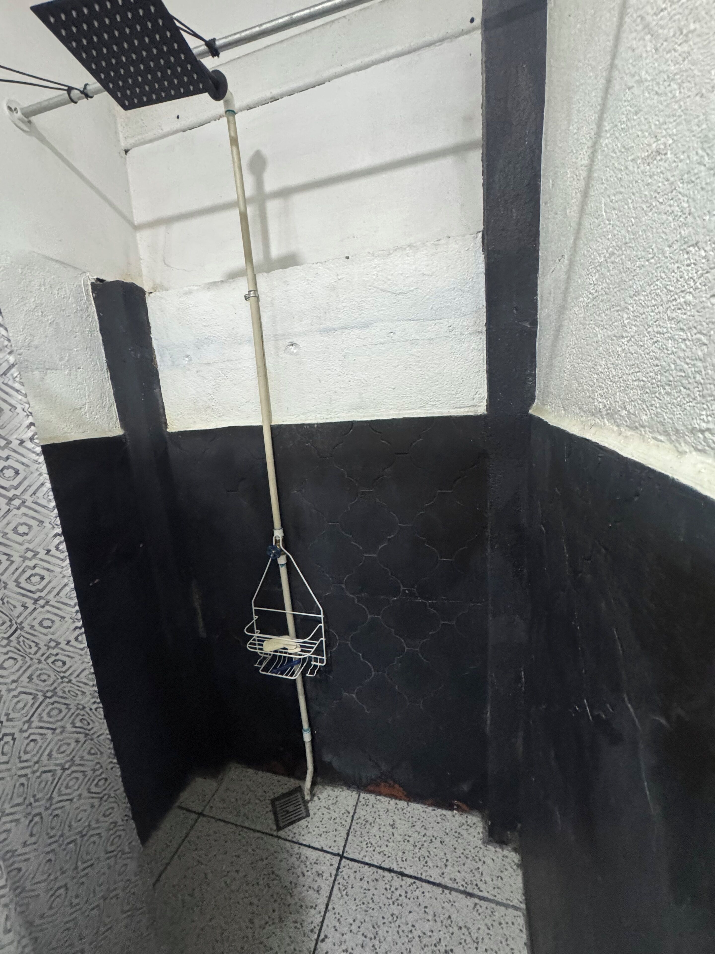 Una esquina de una habitación con pared blanco y negro, una tubería blanca y un estante metálico con un objeto blanco.