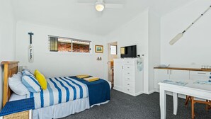 Ein Schlafzimmer mit Bett, Schreibtisch, Fernseher und einem Fenster mit Vorhängen.