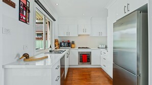 Une cuisine moderne avec des meubles blancs, un réfrigérateur en acier inoxydable, un plan de travail en bois et une fenêtre équipée de stores.