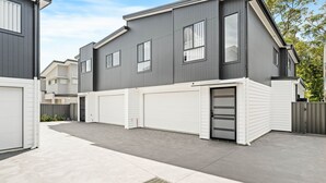 A modern two-story residential building with a grey exterior, white garage doors, and a concrete driveway. - La Casa by the Sea, Jervis Bay (Huskisson)