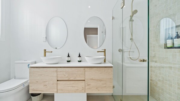Un baño moderno con dos lavamanos, un inodoro, cabina de ducha de vidrio y un espejo.