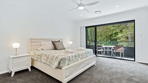 A modern bedroom with a large bed, bedside tables, a ceiling fan, and a balcony with outdoor seating. - La Casa by the Sea, Jervis Bay (Huskisson)