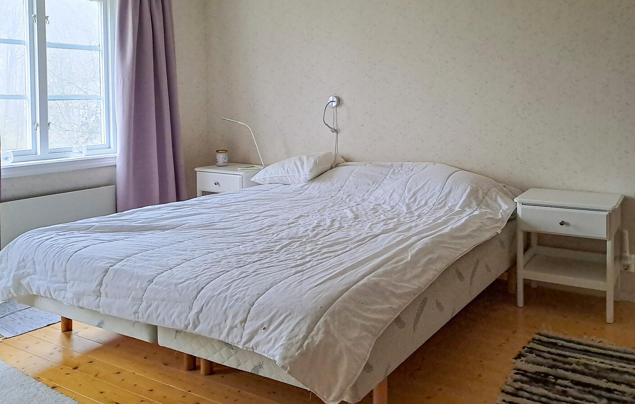 Une chambre à coucher avec un lit, une table de chevet, une lampe et une fenêtre avec des rideaux.