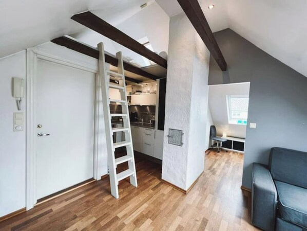 Um apartamento estilo loft com vigas de madeira aparentes, área de cozinha, espaço de estar com sofá e escada para um mezanino.