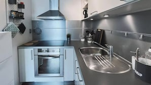 Une cuisine moderne dotée d’appareils électroménagers en acier inoxydable, d’un four encastré, d’une hotte de cuisine de grande taille et d’un élégant plan de travail noir.